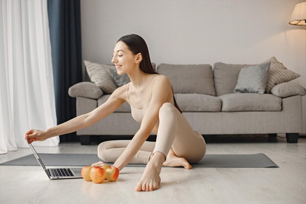 Mujer joven fitness sentada en una alfombra de yoga en casa y usando una computadora portátil