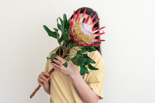 Una mujer joven con flor protea sobre un fondo blanco.