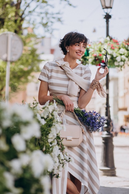 Mujer joven con flores caminando en la ciudad