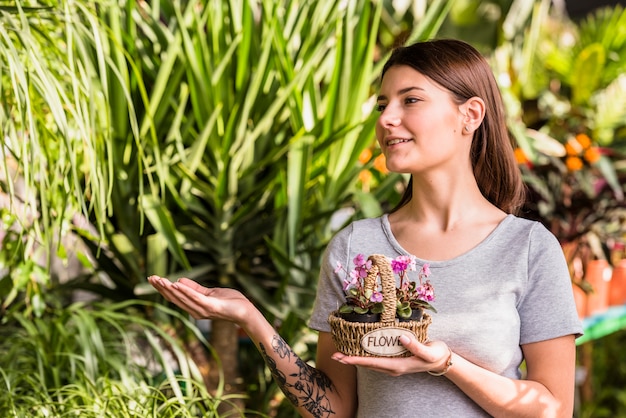 Mujer joven con flores en la cesta que muestra en las plantas verdes