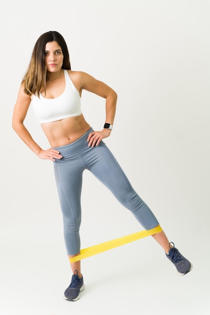 Mujer joven en forma en ropa deportiva trabajando en su cuerpo delgado y tonificado. Atleta femenina con abdominales fuertes ejerciendo sus piernas con una banda de resistencia