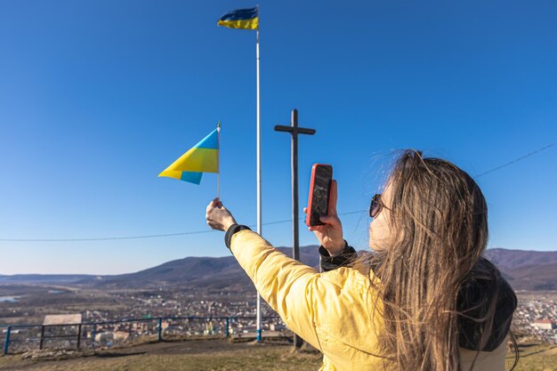 Una mujer joven fotografía la bandera de ucrania con el telón de fondo de la ciudad