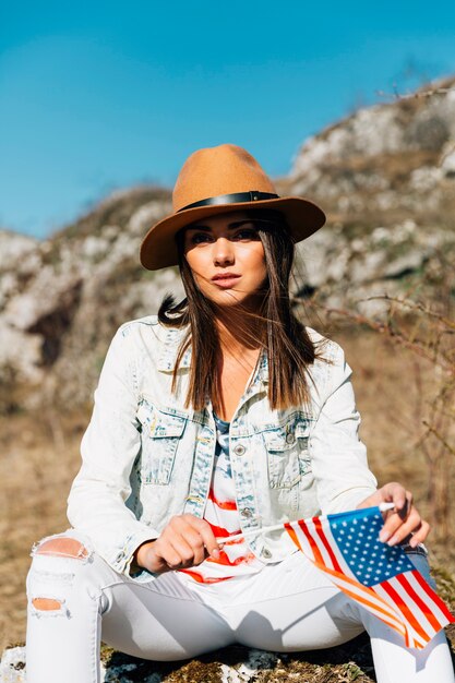 Mujer joven fresca sentada en piedra con la bandera de Estados Unidos