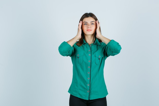 Mujer joven frotando sus sienes en camisa verde y mirando relajado. vista frontal.