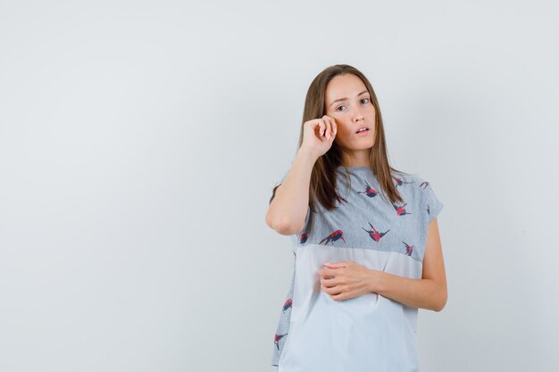 Mujer joven frotándose los ojos para limpiar la lágrima en la camiseta, vista frontal.