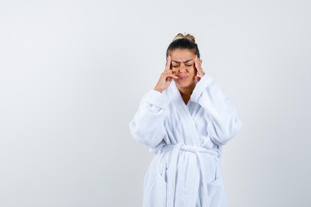 Mujer joven frotándose las sienes en bata de baño y mirando fatigado