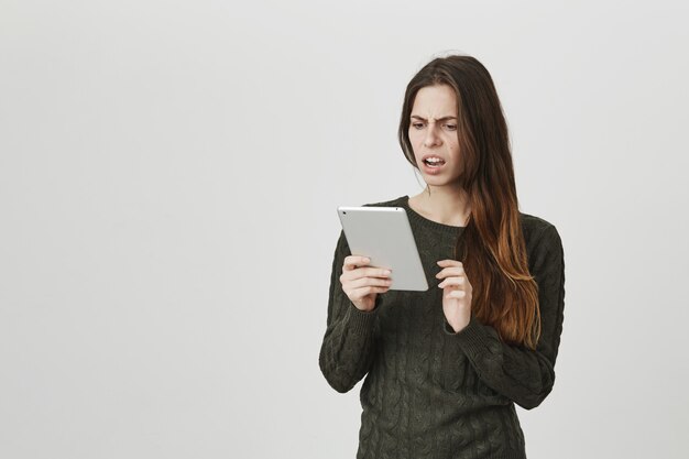 Mujer joven frustrada y conmocionada mirando la pantalla de la tableta digital