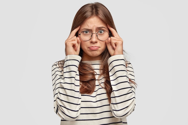 Mujer joven frustrada con gafas posando contra la pared blanca