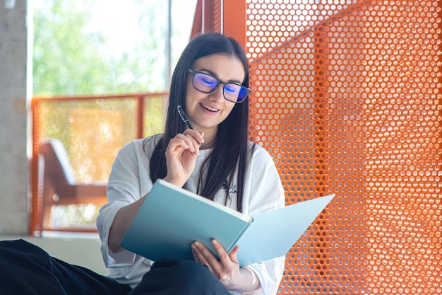 Foto gratuita mujer joven con gafas y cuaderno en concepto de estudio interior moderno