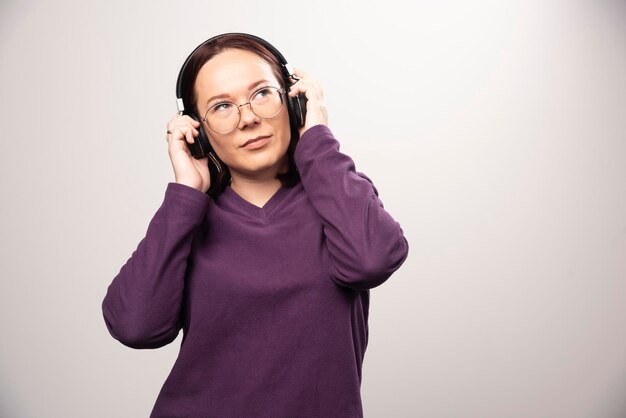 Mujer joven con gafas escuchando música en auriculares sobre un fondo blanco. Foto de alta calidad