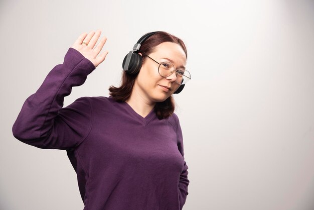 Mujer joven con gafas escuchando música en auriculares sobre un fondo blanco. Foto de alta calidad