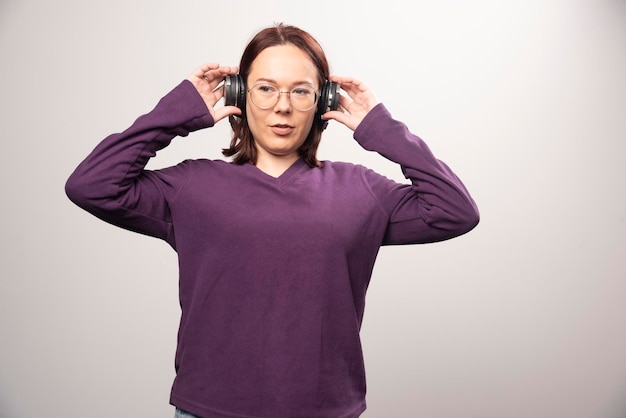 Mujer joven con gafas escuchando música en auriculares sobre un fondo blanco. Foto de alta calidad