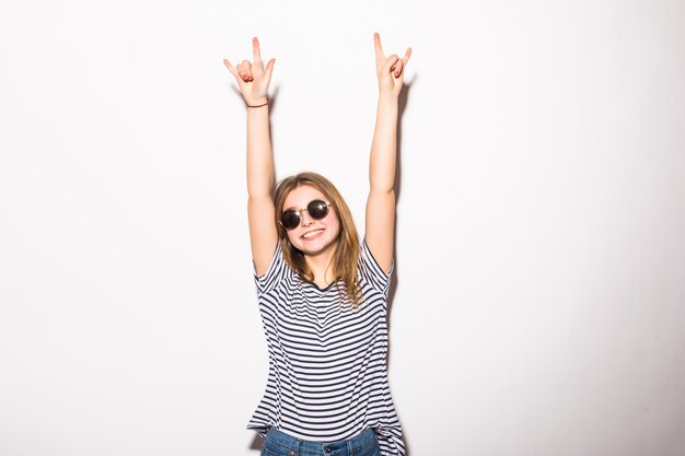 Mujer joven con gafas de sol dando el signo de Rock and Roll aislado en la pared blanca