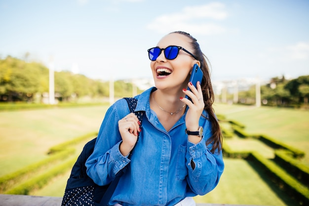 Mujer joven con gafas de sol hablando por un móvil contra un fondo de planta