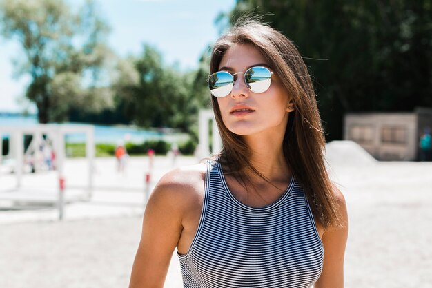 Mujer joven en gafas de sol de pie en la playa