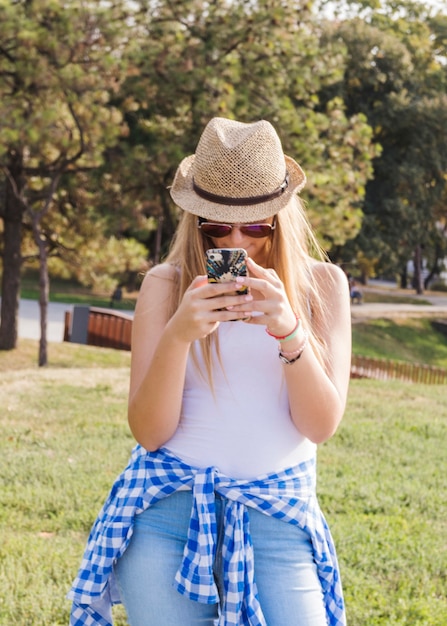 Foto gratuita mujer joven con gafas de sol y sombrero mediante teléfono móvil