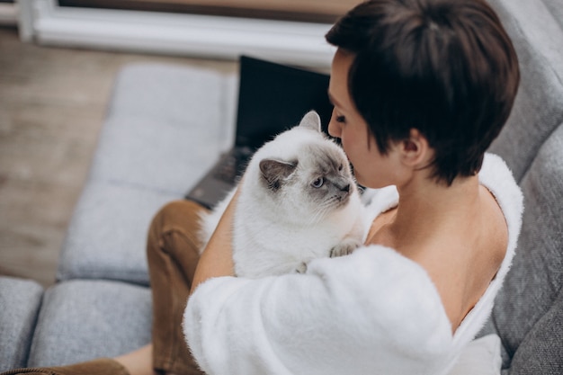 Mujer joven con gato trabajando en el portátil desde casa