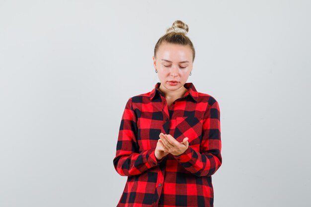 Mujer joven gesticulando como usando un teléfono móvil en camisa a cuadros y mirando ocupado