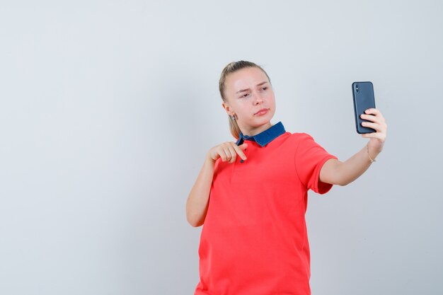 Mujer joven gesticulando mientras toma selfie en camiseta y parece seguro