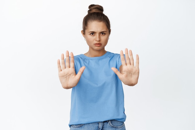 Foto gratuita mujer joven gesticulando parada, diciendo que no, estirando las manos para prohibir algo malo, de pie en blanco