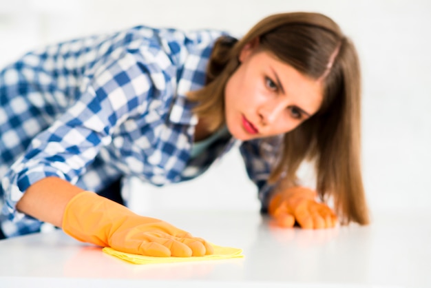 Mujer joven con guantes de protección limpiando el escritorio blanco