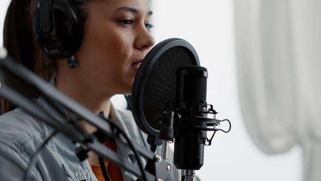 Mujer joven hablando con la audiencia mientras usa un micrófono profesional. Presentador de programas de radio en vivo por Internet que presenta las últimas noticias del día mientras se sienta en el estudio con auriculares modernos.