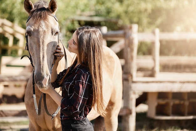 Mujer joven hablando con su caballo en un rancho. Buena oportunidad profesional trabajando al aire libre con animales.