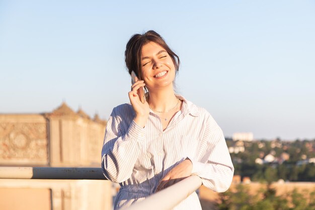 Una mujer joven hablando por teléfono en el balcón al atardecer.