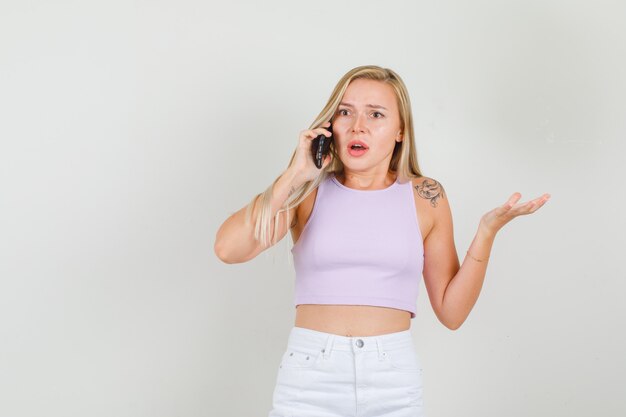 Mujer joven hablando por teléfono en camiseta, mini falda y mirando sorprendido