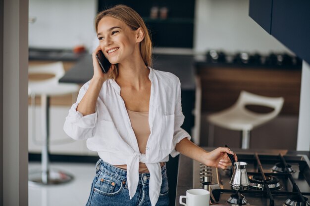 Mujer joven hablando por teléfono y haciendo café por la mañana