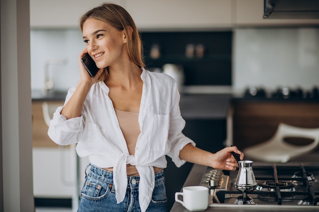 Mujer joven hablando por teléfono y haciendo café por la mañana