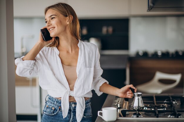 Mujer joven hablando por teléfono y haciendo café por la mañana