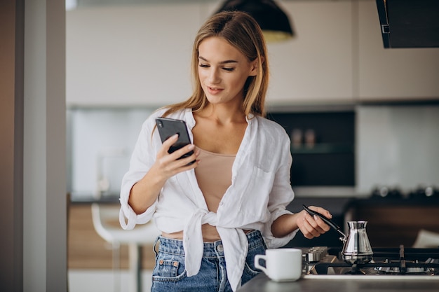 Mujer joven hablando por teléfono y haciendo café por la mañana