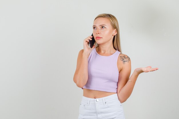 Mujer joven hablando por teléfono inteligente en camiseta, mini falda