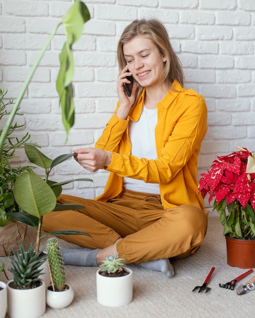 Foto gratuita mujer joven hablando por teléfono junto a su planta