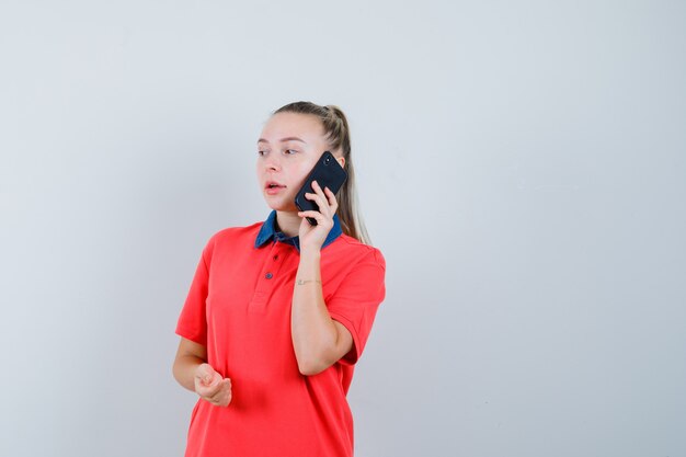 Mujer joven hablando por teléfono móvil en camiseta y mirando pensativo