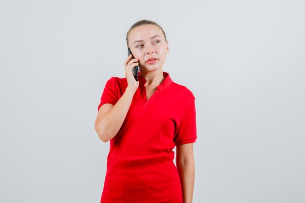 Mujer joven hablando por teléfono móvil en camiseta roja y mirando pensativo