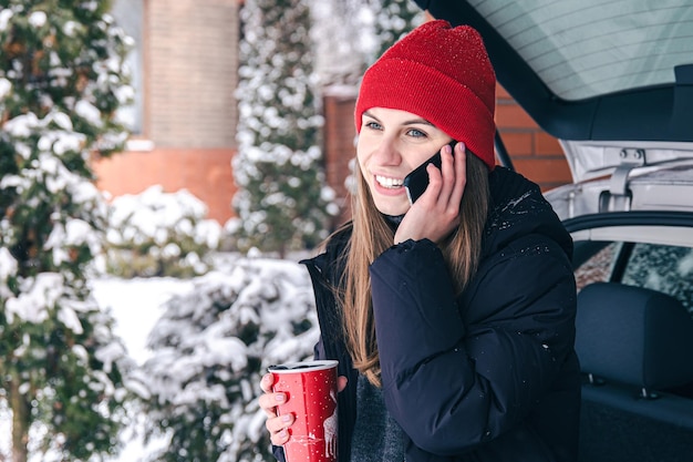 Mujer joven hablando por teléfono de pie cerca del coche en invierno