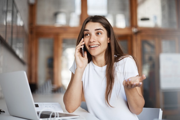 Mujer joven hablando por teléfono sorprendida positivamente al descubrir que su novio viene a la ciudad.