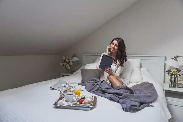 Foto gratuita mujer joven hablando por teléfono y sujetando una tableta