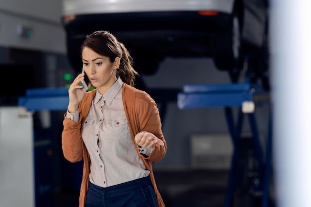 Mujer joven hablando por teléfono en el taller de reparación de automóviles