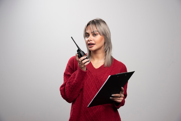 Mujer joven hablando con transceptor de radio y mirando a cámara.