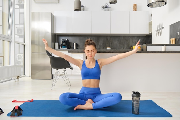 Foto gratuita mujer joven haciendo deportes meditando en una estera de yoga en casa toma las manos de lado y respira ejercicios relajantes y conscientes