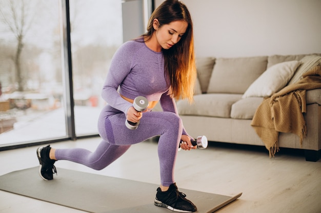 Mujer joven haciendo ejercicio con pesas en casa en mat