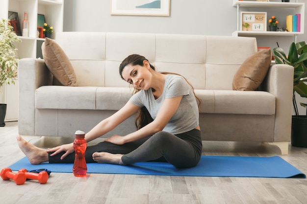 Mujer joven haciendo ejercicio sobre una estera de yoga delante del sofá en la sala de estar