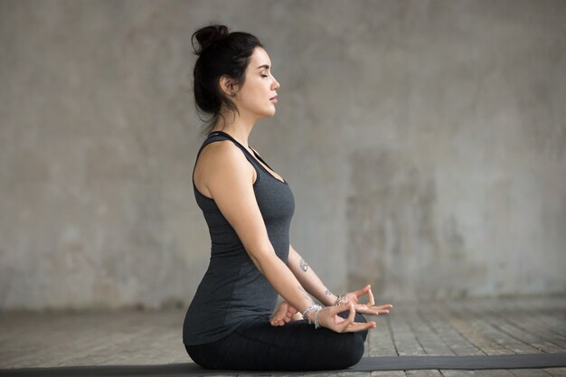 Mujer joven haciendo ejercicio Sukhasana, vista lateral