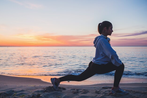 Mujer joven haciendo ejercicios deportivos en la playa del amanecer en la mañana