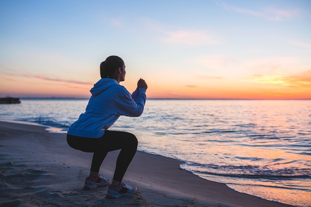 Mujer joven haciendo ejercicios deportivos en la playa del amanecer en la mañana