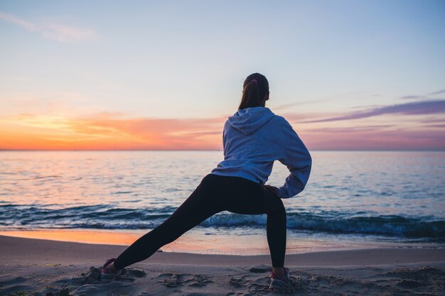 Mujer joven haciendo ejercicios deportivos en la playa del amanecer en la mañana