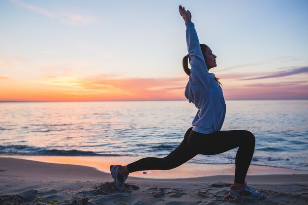 Mujer joven haciendo ejercicios deportivos en la playa del amanecer en la mañana